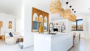Una cocina moderna con una isla central, un espejo grande y lámparas colgantes de mimbre.