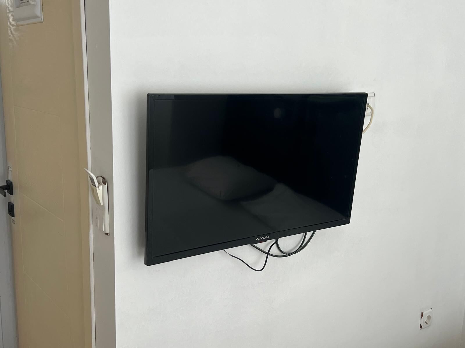 Una TV a schermo piatto montata su una parete bianca, con una presa di corrente e un sistema di gestione dei cavi visibili.