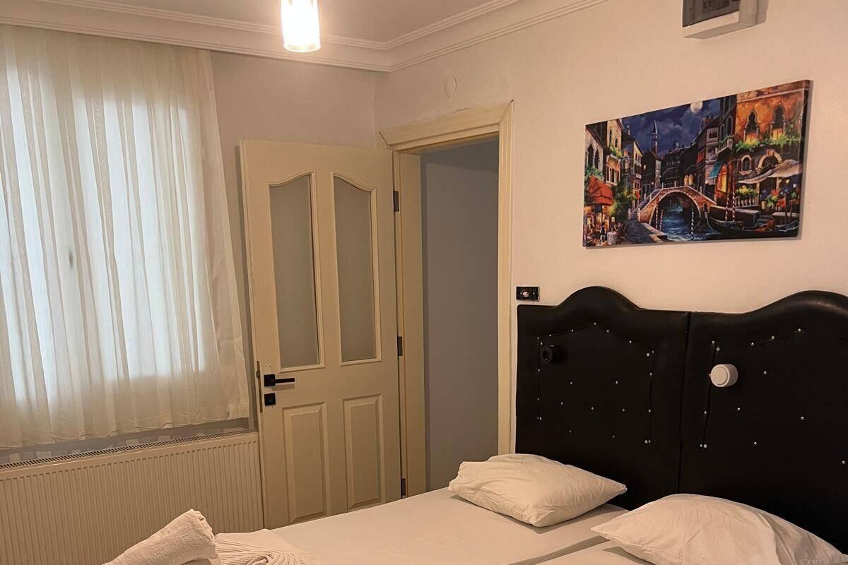 Uma cama de casal com lençóis brancos, uma cabeceira preta e um quadro de uma paisagem urbana na parede.