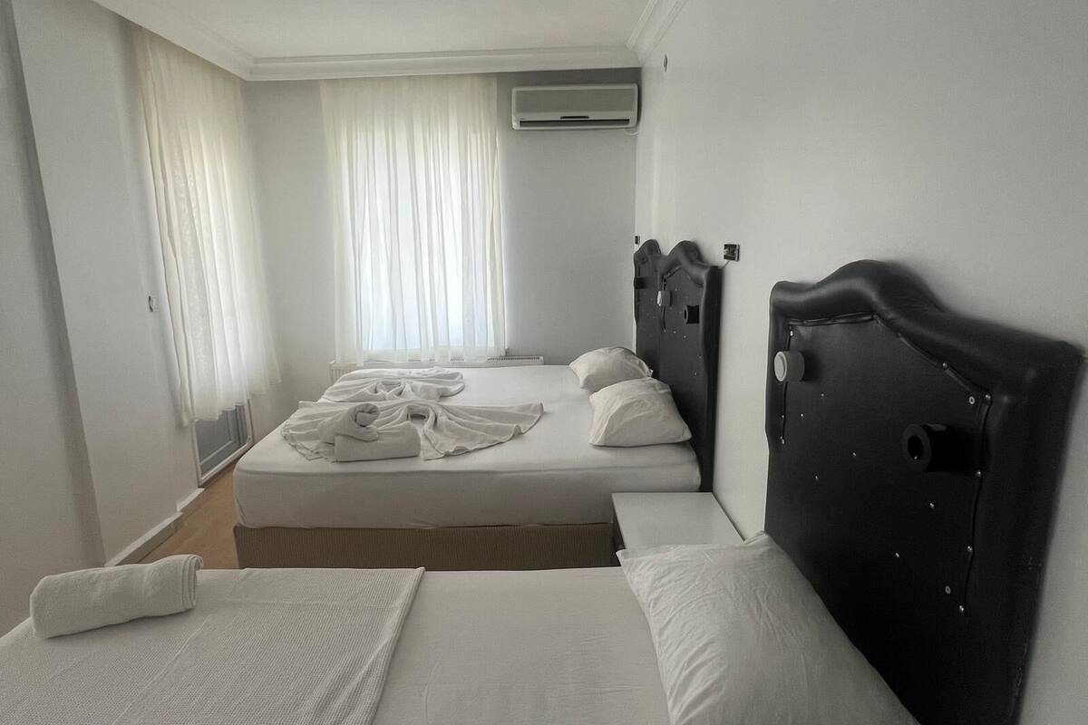 Quarto de hotel com uma cama de casal, uma cama individual adicional, cabeceira, janela com cortinas e ar condicionado.