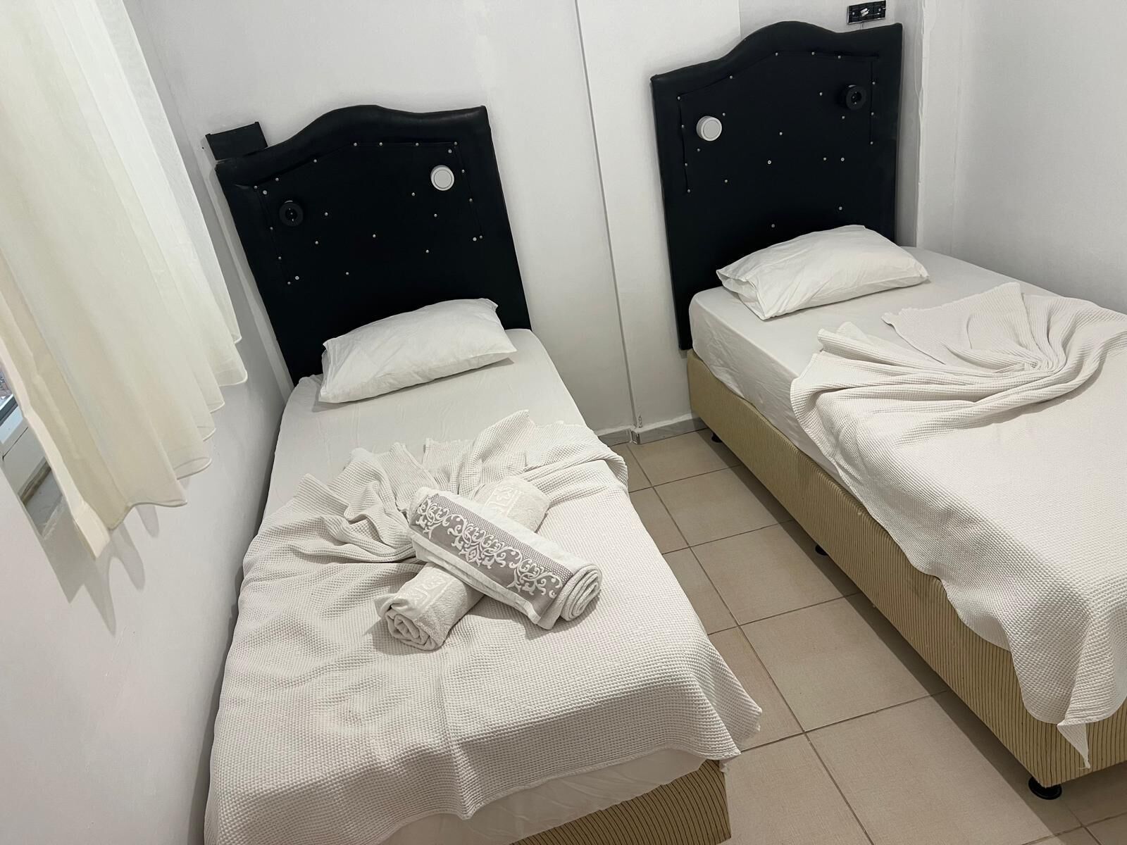 Two single beds with white linens, a black headboard, and a white curtain.