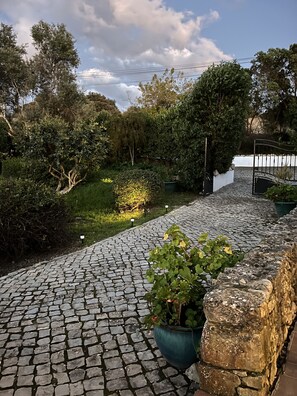 A cobblestone pathway, greenery, and a metal gate. - Casa no Limoeiro, Stylish Retreat (Loulé)