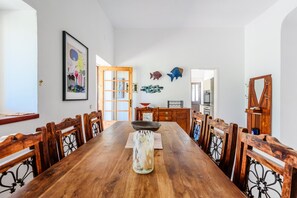 A dining room with a long wooden table, chairs, a vase, and wall decorations including fish and a framed picture. - Casa no Limoeiro, Stylish Retreat (Loulé)