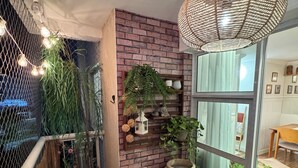 Ein Balkon mit Backsteinwand, hängenden Pflanzen, einer großen Vase und einer Weidenkorbschirm.'