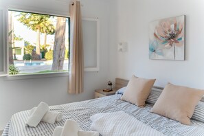 A bedroom with a bed, pillows, a bedside table, a window with curtains, and a painting on the wall. - Can Xala - Flat with a swimming pool near the sea (Ciutadella de Menorca)