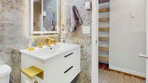 Un baño con pared de mármol, un lavabo blanco con detalles dorados, un espejo y una toalla colgada en la pared.