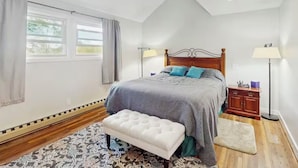 Un dormitorio con cama, mesitas de noche, un banco, una ventana y una lámpara de pie.