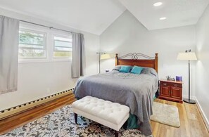 Ein Schlafzimmer mit Bett, Nachttischen, einer Bank, einem Fenster und einer Stehlampe.