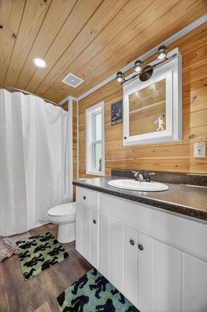 Une salle de bain avec un plafond en bois, un lavabo blanc et un rideau de douche.