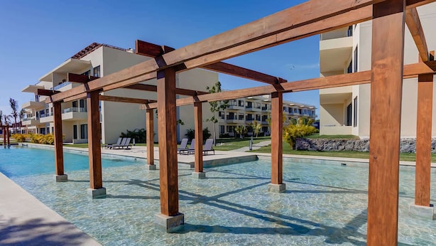 A clear pool with wooden pergolas, lounge chairs, and a building with balconies in the background. - Pacific coast retreat w/ kayak, bikes & pool (Tondoroque)