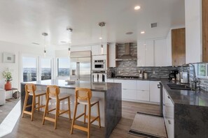 A modern kitchen with a central island, bar stools, and a view of the city. - Modern 5BR Oasis - City Views, Gym & Gated Parking (San Diego)