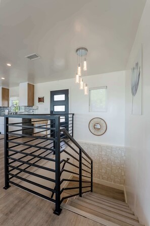 A kitchen with a central island, a staircase, and a wall-mounted mirror. - Modern 5BR Oasis - City Views, Gym & Gated Parking (San Diego)