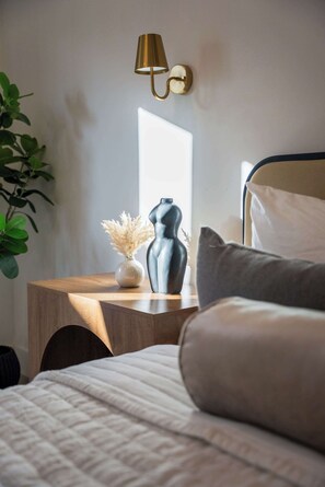 A bedroom with a bed, a bedside table with a lamp, a vase with dried flowers, and a plant. - Modern 5BR Oasis - City Views, Gym & Gated Parking (San Diego)