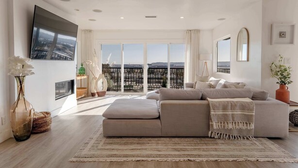 Ein modernes Wohnzimmer mit einem großen Fenster, einem Flachbildfernseher und einem beigefarbenen Sofa.