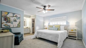 A bedroom with a bed, a desk, a chair, a ceiling fan, and a painting on the wall. - The Coventry — A Family Retreat Near LSU 4BR/2BA w Game Room & Basketball Goal (Baton Rouge)