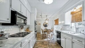 A kitchen with white cabinets, a stove, a microwave, and a dining area with a table and chairs. - The Coventry — A Family Retreat Near LSU 4BR/2BA w Game Room & Basketball Goal (Baton Rouge)