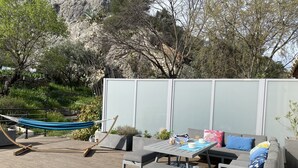 An outdoor patio with a hammock, grey cushioned seating, a table with a blue patterned rug, and a white privacy screen. - Quiet studio at the foot of St Jacques hill,a stone's throw from the city center (Cavaillon)