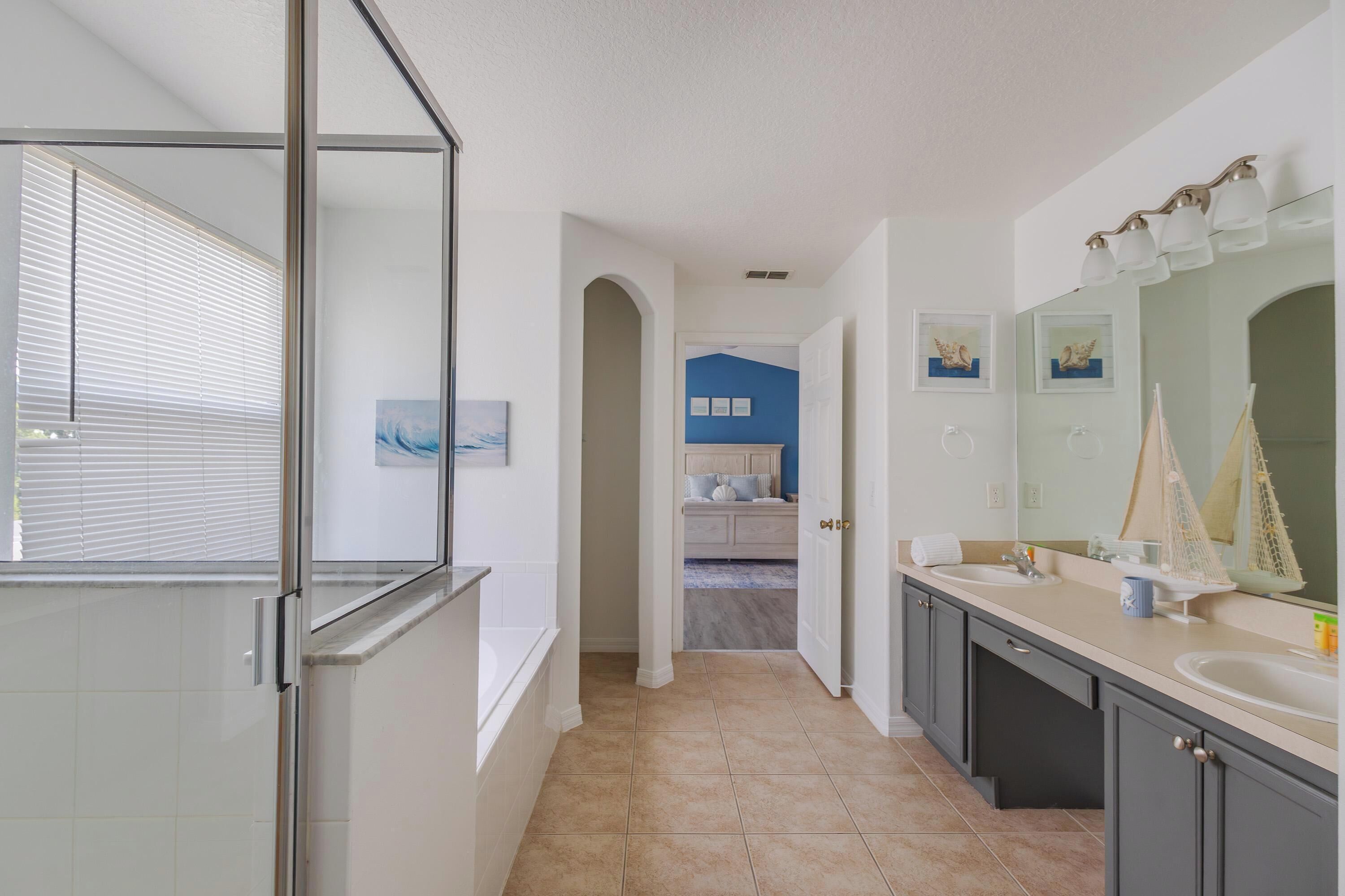Une salle de bain moderne dotée d’une douche à parois de verre, d’un meuble-lavabo avec un grand miroir et donnant sur la chambre à coucher.