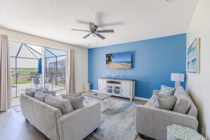 A living room with a ceiling fan, a TV mounted on the wall, a sofa, a coffee table, and a view of the outdoors through large glass doors. - Sunset Paradise Villa | Private South Facing Pool & Spa | Near Disney (Davenport)