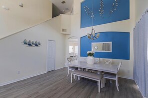 A dining area with a white table and bench, a chandelier, and a blue accent wall. - Sunset Paradise Villa | Private South Facing Pool & Spa | Near Disney (Davenport)