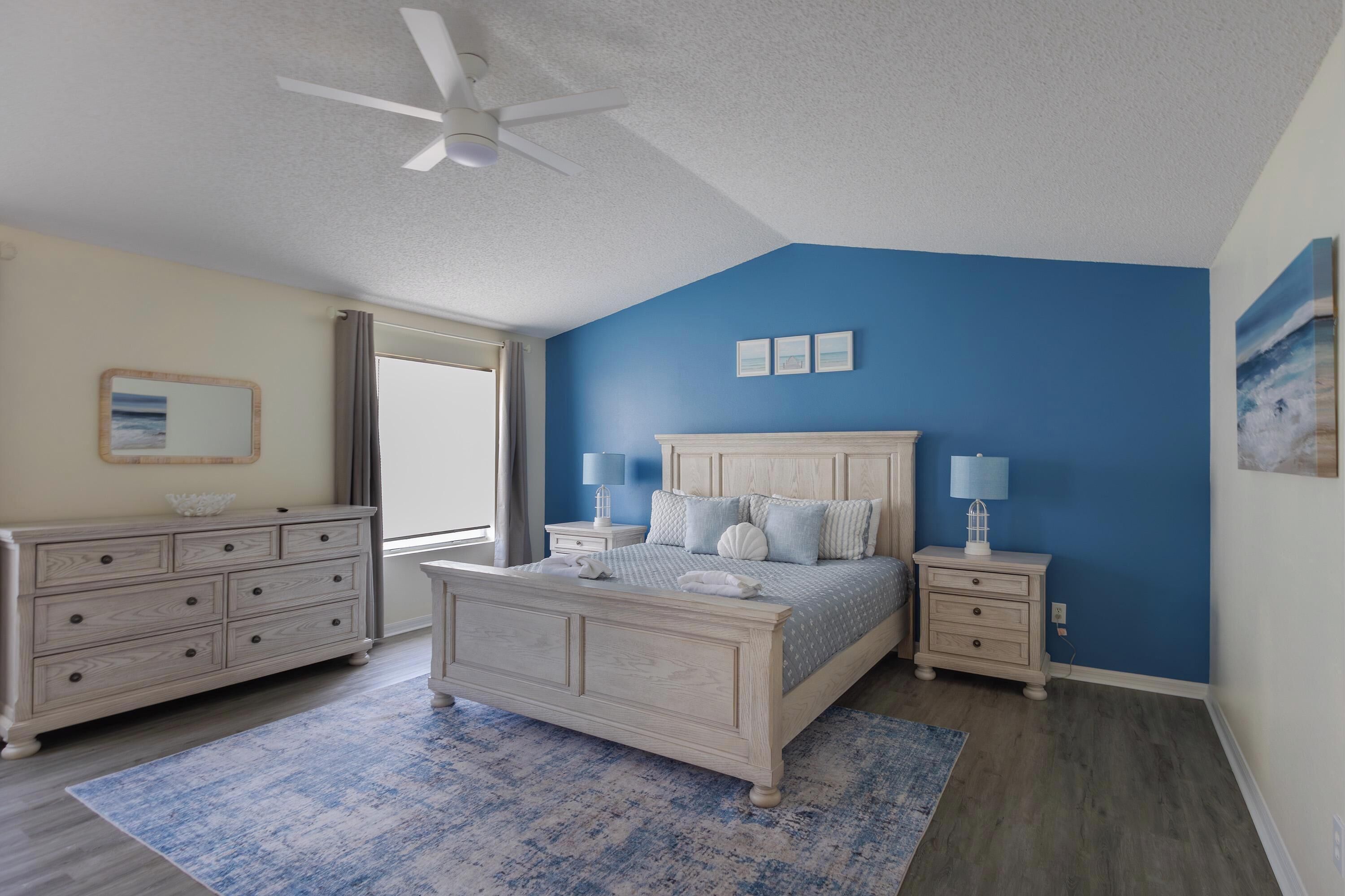 A bedroom with a bed, nightstands, a dresser, a ceiling fan, and a window.