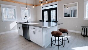 A modern kitchen with a central island, bar stools, and a dining area. - Modern Butterfly - Stylish 3 Bed 3 Bath with Hot Tub! Rumbling Bald Amenities! (Lake Lure)