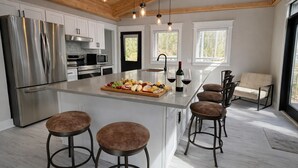 A modern kitchen with a central island, stainless steel appliances, and a seating area with bar stools. - Modern Butterfly - Stylish 3 Bed 3 Bath with Hot Tub! Rumbling Bald Amenities! (Lake Lure)