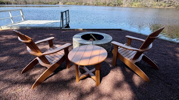 A lakeside deck with Adirondack chairs, a fire pit, and a dock extending into the water.