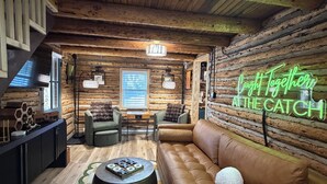 A cozy log cabin interior with a leather sofa, a round coffee table, and a neon sign reading 'Caught Together At The Catch'.