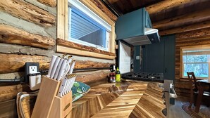A rustic kitchen with wooden walls, a herringbone-patterned floor, a knife block, a stove, and a window with a view.