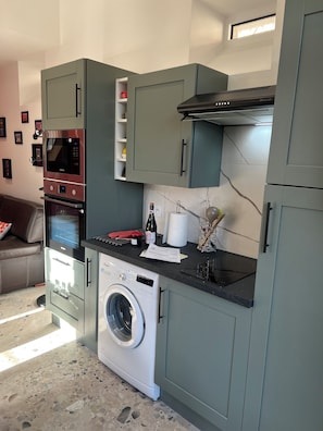 A compact kitchen with a washing machine, microwave, and oven. - Maison proche mer (Reviers)