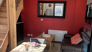 A modern kitchen with a built-in oven, a dining area with a wooden table and chairs, and a red accent wall. - Maison proche mer (Reviers)