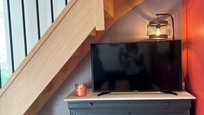 A staircase with wooden railings, a flat-screen TV on a cabinet, a lit candle, and a red wall. - Maison proche mer (Reviers)