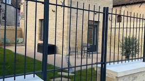A stone building with a red-tiled roof, a black metal gate, and a small patio area with outdoor furniture. - Maison proche mer (Reviers)