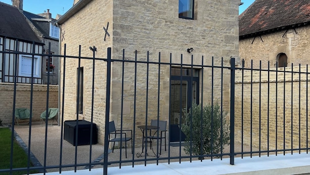 A stone building with a black metal fence, a small window, and outdoor seating. - Maison proche mer (Reviers)