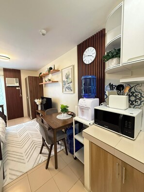 A compact kitchen with a microwave, water dispenser, and a clock on the wall.