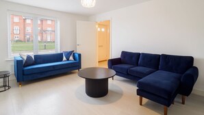 Een moderne woonkamer met twee banken, een salontafel en uitzicht op een gebouw van rode baksteen door grote ramen.