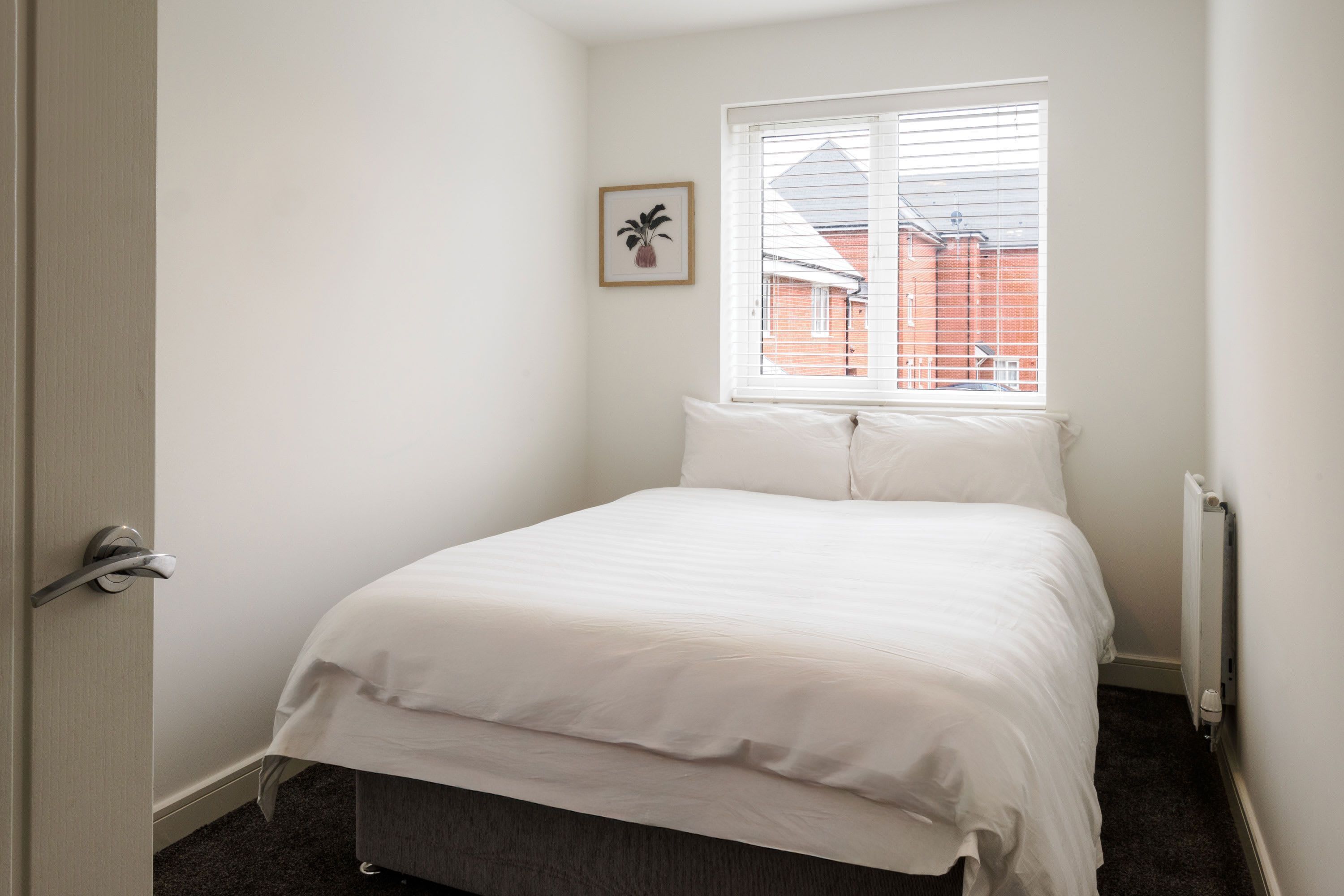 Un dormitorio con cama, ventana, radiador y puerta.