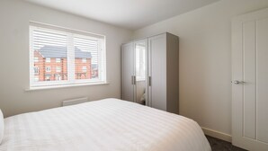 Een slaapkamer met een bed, een kledingkast, een raam met zonwering en een radiator.