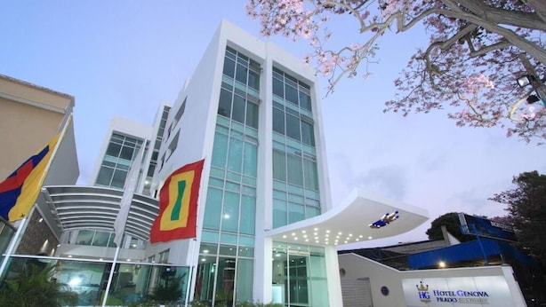 A modern hotel building with large glass windows, a prominent flag, and a sign indicating it is the Hotel Genova Prado. - HOTEL GENOVA PRADO (Barranquilla)