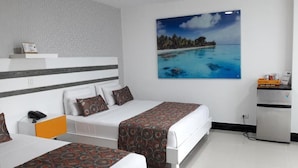 A hotel room with two beds, a desk, a refrigerator, and a painting of a beach. - HOTEL GENOVA PRADO (Barranquilla)