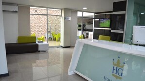 A hotel reception area with a modern design, a reception desk, and a seating area with chairs. - HOTEL GENOVA PRADO (Barranquilla)