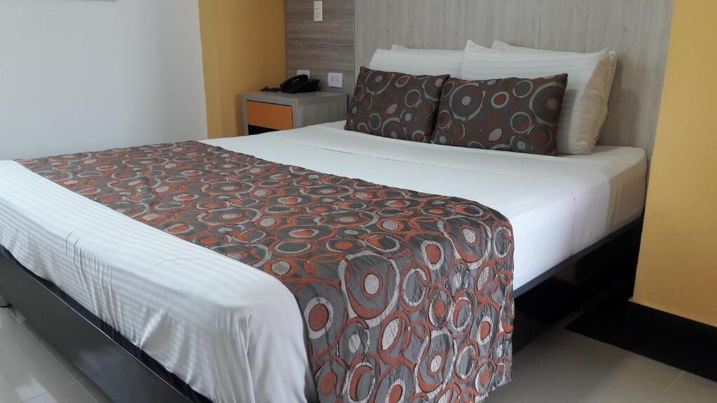 Hotellihuone, jossa on sänky, yöpöytä ja seinälle asennettu puhelin.
