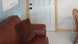 A room with a brown leather sofa, a wooden chair, a white door with a frosted glass panel, and a light blue wall. - - Love and Tranquility (Room E and Room C)  (Tampa)
