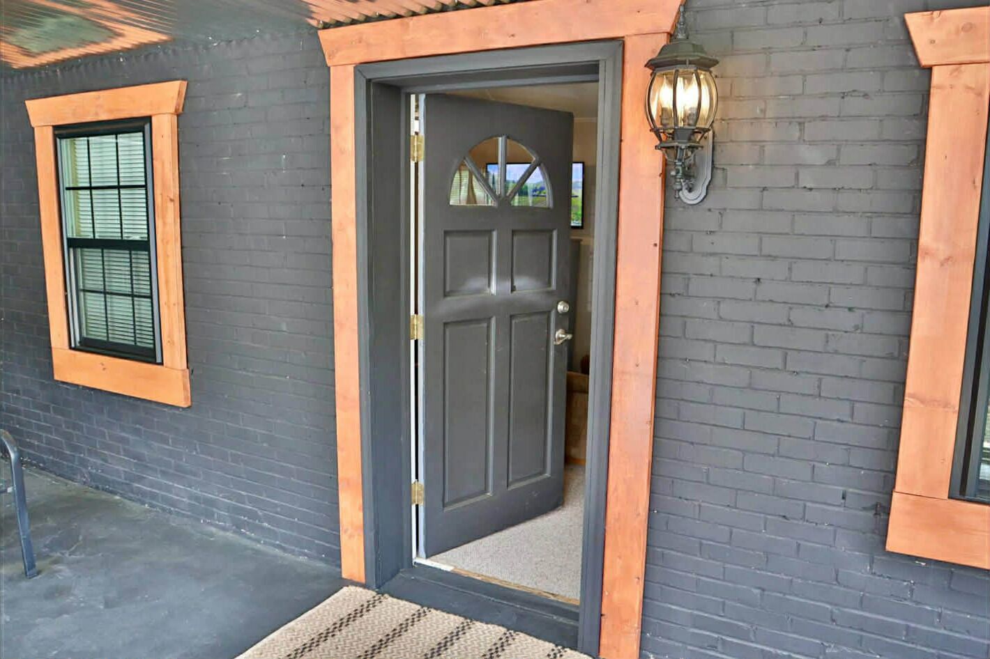 A dark grey door with a wooden frame, a small window with blinds, and a wall-mounted light fixture.