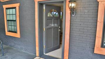 A dark grey door with a wooden frame, a small window with blinds, and a wall-mounted light fixture.