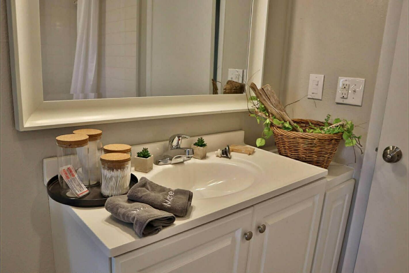 A bathroom with a white sink, a mirror, a basket of plants, and a towel rack with towels.