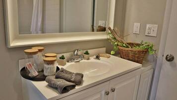 A bathroom with a white sink, a mirror, a basket of plants, and a towel rack with towels.