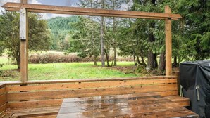 A wooden deck with benches and a table, surrounded by trees and a grassy area. - Forest River Farmhouse Retreat (Fall Creek)