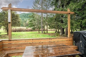 A wooden deck with benches and a table, surrounded by trees and a grassy area. - Forest River Farmhouse Retreat (Fall Creek)